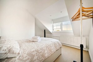 Ein Schlafzimmer mit schrägen Wänden, einem Bett mit gemustertem Überwurf, einem Heizkörper und einem Fenster mit Blick.