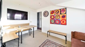 A modern room with a wooden table, benches, a TV, and a colorful abstract painting. - Chelsea Loft - Stylish Sanctuary (London)