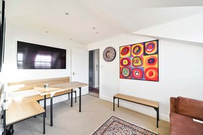 A modern room with a wooden table, benches, a TV, and a colorful abstract painting. - Chelsea Loft - Stylish Sanctuary (London)