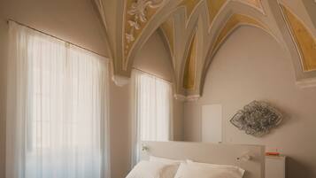 Quarto com cama grande, teto ornamentado e um detalhe decorativo na parede.