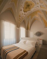 Quarto com cama grande, teto ornamentado e um detalhe decorativo na parede.