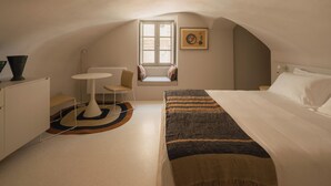 Un dormitorio con cama, una mesita, una silla y una ventana.