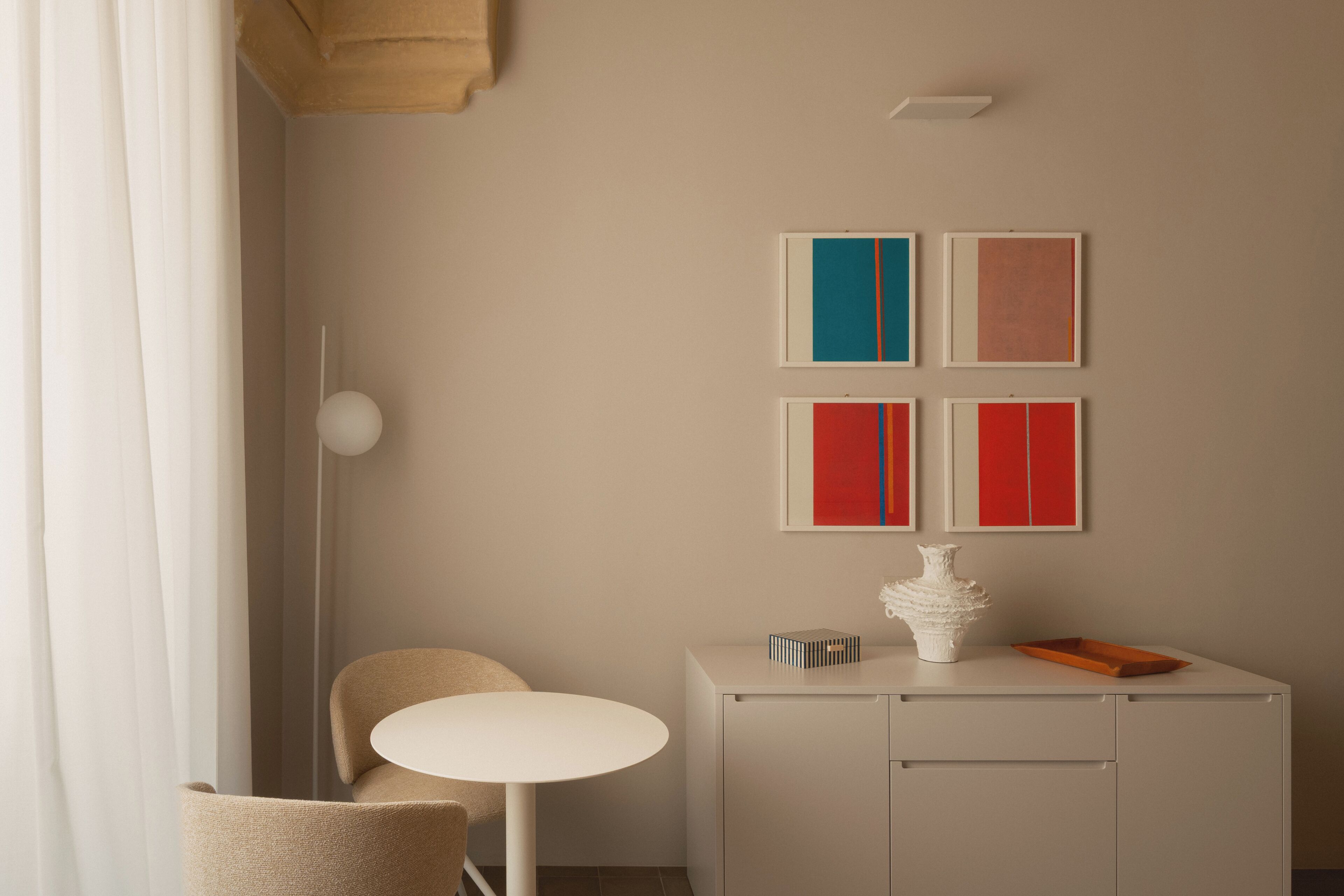 Una habitación con una mesa redonda, una silla, un aparador con un jarrón, y cuatro obras de arte enmarcadas en la pared.