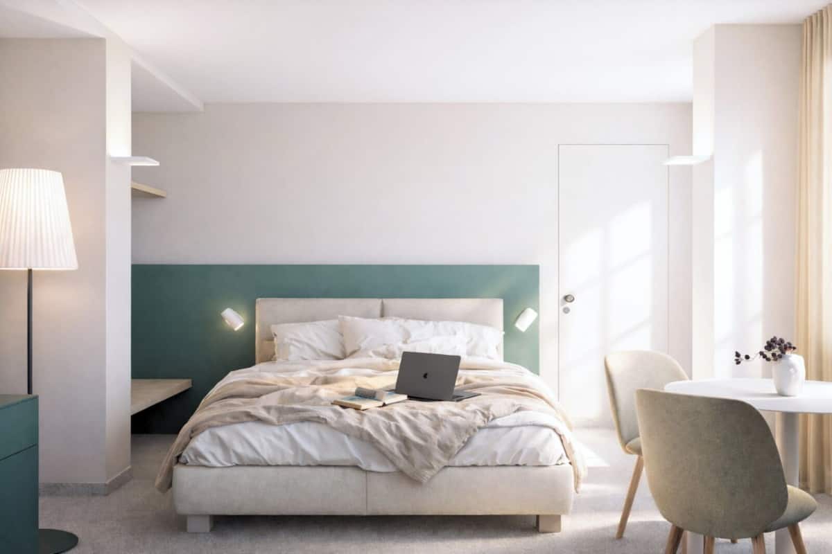 A neatly arranged hotel room with a bed, a desk, a chair, and a lamp.
