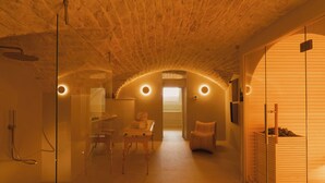 Un cuarto de spa con techo de piedra, cabina de ducha de vidrio, banca de madera y una pequeña mesa con toallas.