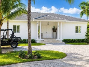 A white building with a tiled roof, a paved driveway, and a parked vehicle.