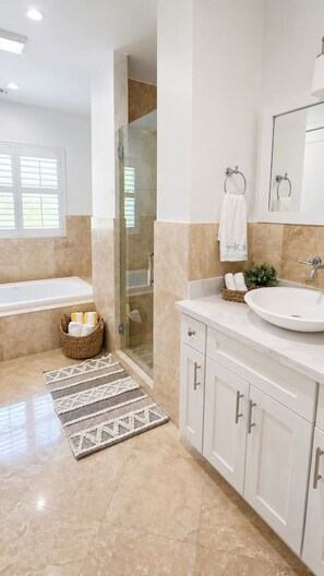A bathroom with a bathtub, a glass shower enclosure, a sink, and a mirror.