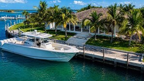 Un barco amarrado en un puerto deportivo, con un edificio blanco y palmeras al fondo.