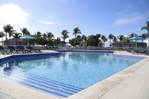 A swimming pool with lounge chairs and umbrellas, surrounded by palm trees and a clear sky.