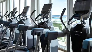 Varias bicicletas estáticas en un gimnasio con ventanas amplias y vista al mar.
