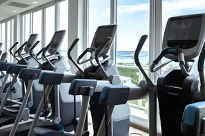 Une rangée de vélos d’appartement dans une salle de sport dotée de grandes fenêtres et offrant une vue sur la mer.