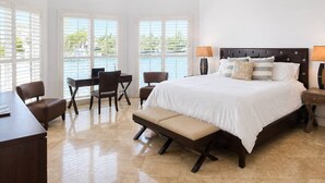 Un dormitorio con cama, dos sillas, un escritorio, un banco y vistas al exterior a través de amplios ventanales.