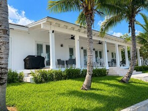 A white building with a covered patio, palm trees, and a grill.