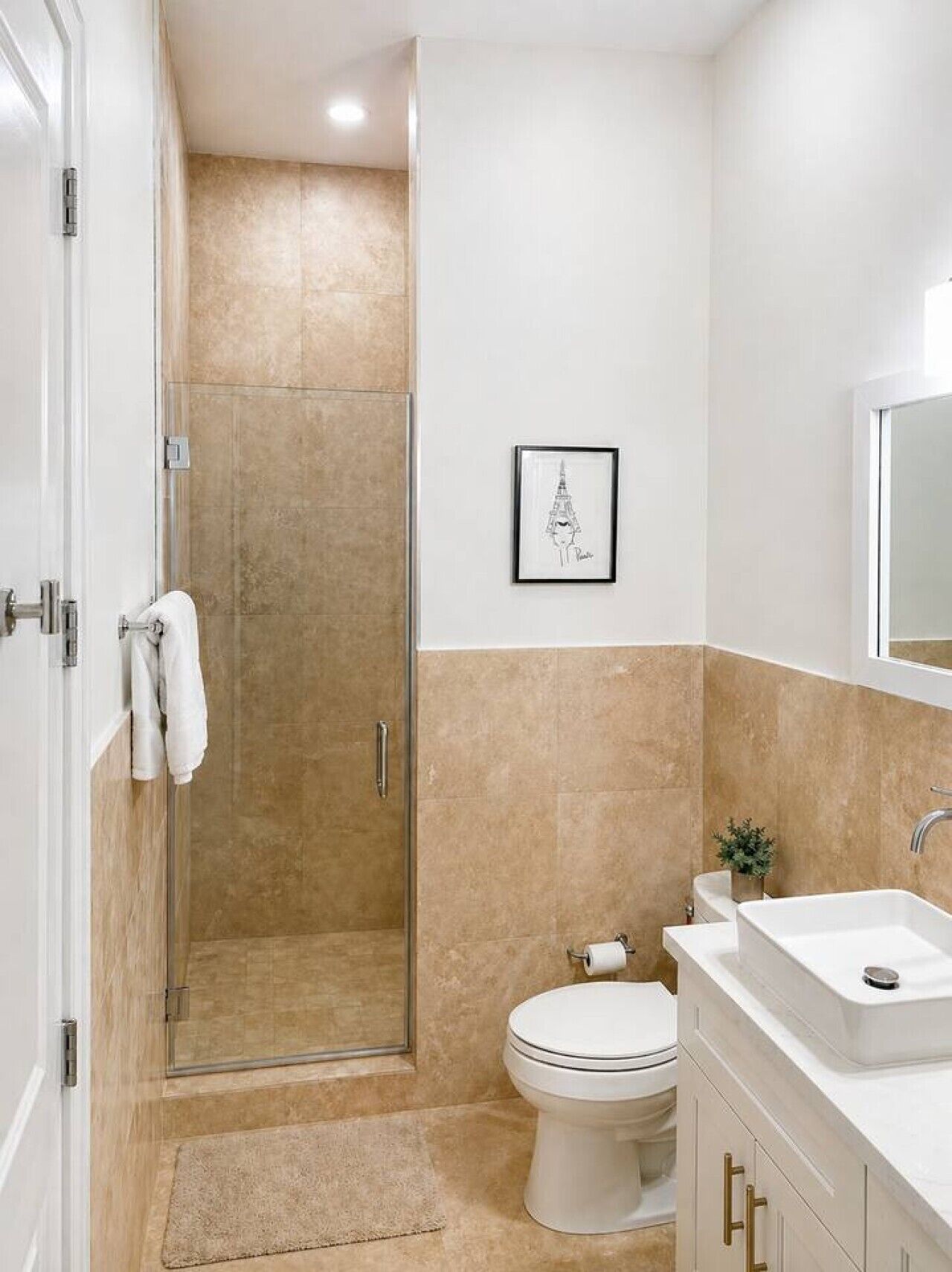 A bathroom with a shower, toilet, sink, and a framed picture on the wall.