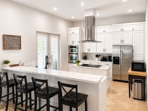 A modern kitchen with white cabinetry, a stainless steel range hood, and a central island with bar stools.
