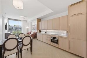 A modern kitchen with light wood cabinets, a marble countertop, and a dining area with a table and chairs. - Stylish Wynwood Apartment with Resort Pool and Gym (Miami)