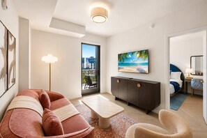 Un salon moderne avec un canapé, une table basse, un téléviseur et un balcon offrant une vue sur la ville.