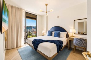 Une chambre d’hôtel avec un lit, un bureau, une chaise, une grande fenêtre et un luminaire au plafond.