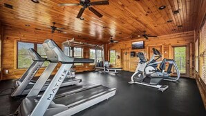 A gym with treadmills, stationary bikes, and weight machines in a cabin with wooden walls and ceiling. - Views Forever | Smoky Mountain Views, Hot Tub, Theater & Game Room (Gatlinburg)