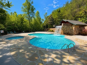 Ein Swimmingpool mit Wasserfall, umgeben von Steinplatten und Bäumen.