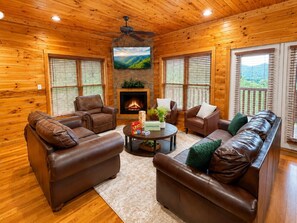 Ein gemütliches Blockhaus-Interieur mit Ledersofas, einem Kamin und einem an der Wand befestigten Fernseher.