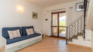 Una habitación con sofá, una mesita, una escalera y una puerta que da a un espacio exterior.