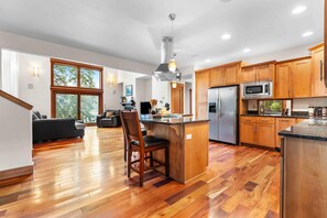 A spacious kitchen with wooden cabinets, a central island, and a dining area with a sofa and chairs. - The Lantern House | Lake Views, Fire Pit & Luxury (Hayden)