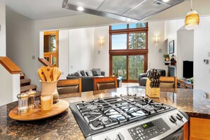 A modern kitchen with a gas stove, wooden countertops, and a dining area with a sofa and coffee table. - The Lantern House | Lake Views, Fire Pit & Luxury (Hayden)
