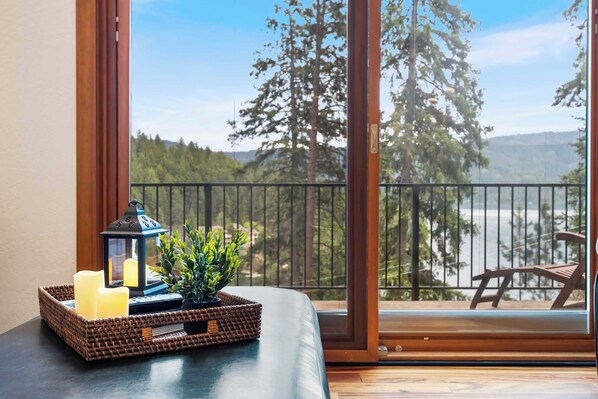 A balcony with a view of trees and a body of water, a wicker tray with candles, and a lantern. - The Lantern House | Lake Views, Fire Pit & Luxury (Hayden)