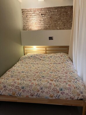 A bedroom with a brick wall, a wooden bed frame, and a floral bedspread. - Large beautiful 1-bedroom studio in Amsterdam center, perfect for your getaway (Amsterdam)