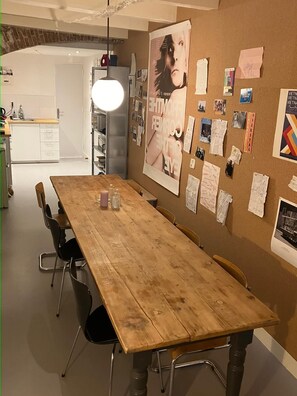 A dining area with a wooden table, chairs, and a corkboard with various papers and photos. - Large beautiful 1-bedroom studio in Amsterdam center, perfect for your getaway (Amsterdam)