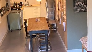 Uma área de refeições com uma mesa e cadeiras de madeira, uma cozinha ao fundo e um tapete estampado no chão.