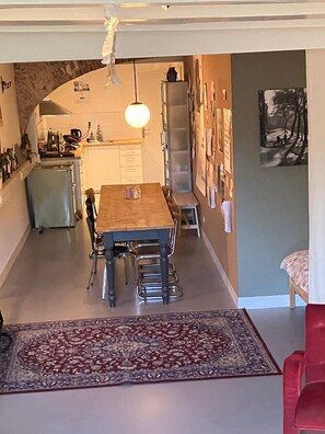 A dining area with a wooden table and chairs, a kitchen in the background, and a patterned rug on the floor. - Large beautiful 1-bedroom studio in Amsterdam center, perfect for your getaway (Amsterdam)