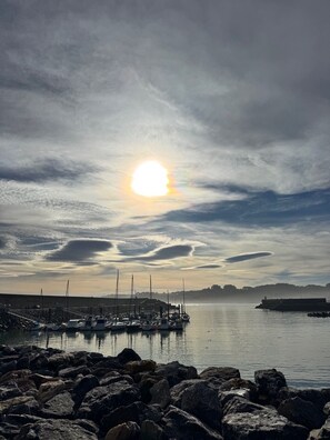 Una marina con barcos amarrados, una costa rocosa y un atardecer al fondo.