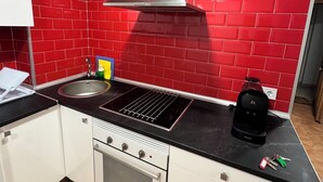 Una cocina con paredes de baldosas rojas, una campana extractora de acero inoxidable, una placa de inducción negra, un horno empotrado y una cafetera.