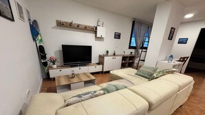 Una sala de estar con sofá, televisor, mesa de centro de madera y un mueble blanco.