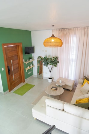 A modern living room with a sofa, a coffee table, a TV, and a potted plant.