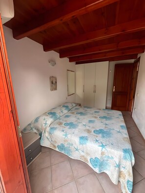 A bedroom with a bed, a wardrobe, a mirror, and a small bedside table.
