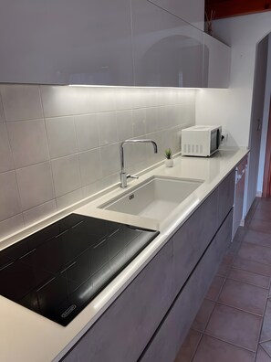 A modern kitchen with a black induction cooktop, a white sink with a chrome faucet, and a microwave on the countertop.