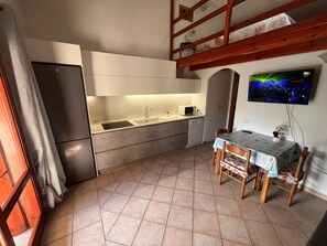 A compact kitchen with a built-in oven, a microwave, and a sink. There is a dining table with chairs and a television mounted on the wall.