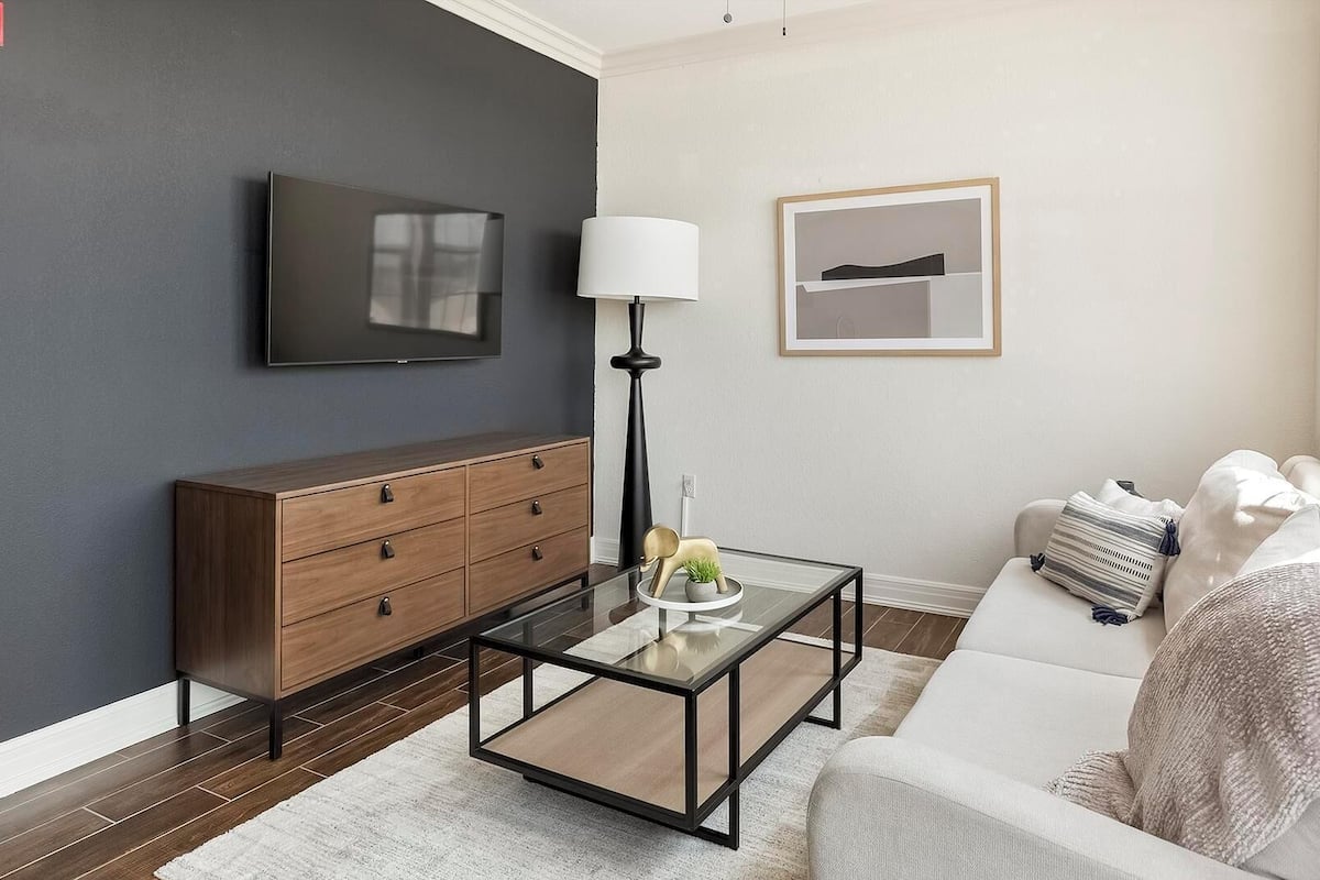 A modern living room with a dark wall, a wooden cabinet, a glass coffee table, a sofa, and a lamp.