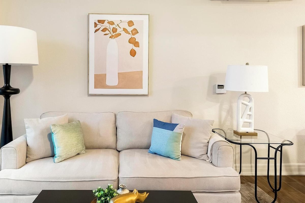 A living room with a sofa, two lamps, a framed artwork, and a coffee table with decorative items.