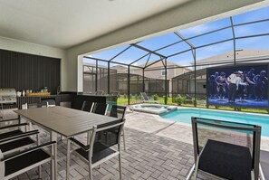 An outdoor patio with a pool, a dining area, and a large screen displaying a show. - Unique Luxury Villa, Pool, Games and Themed Beds (Clermont)