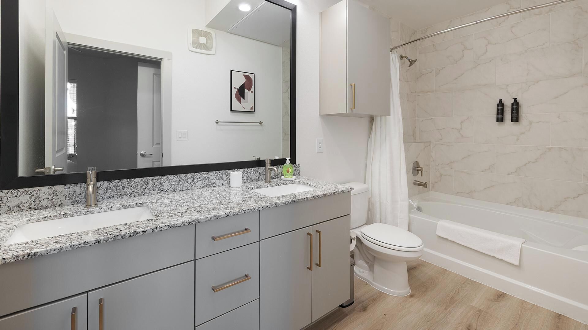 A modern bathroom with a granite countertop, a large mirror, a toilet, and a shower area.