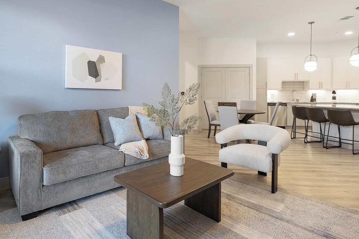 Ein modernes Wohnzimmer mit einem grauen Sofa, einem Couchtisch, einer Lampe und einer Vase mit Zweigen.