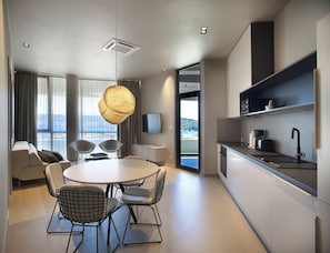 Habitación de hotel moderna con zona de comedor, cocina y un gran ventanal con vistas.