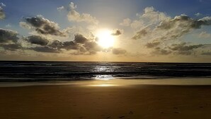 Una spiaggia con il sole che tramonta sull'oceano, creando il profilo delle nuvole.