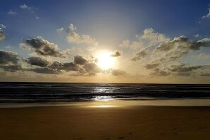 A beach with the sun setting over the ocean, creating a silhouette of clouds. - VG Fun Residence - Praia do Futuro (Fortaleza)