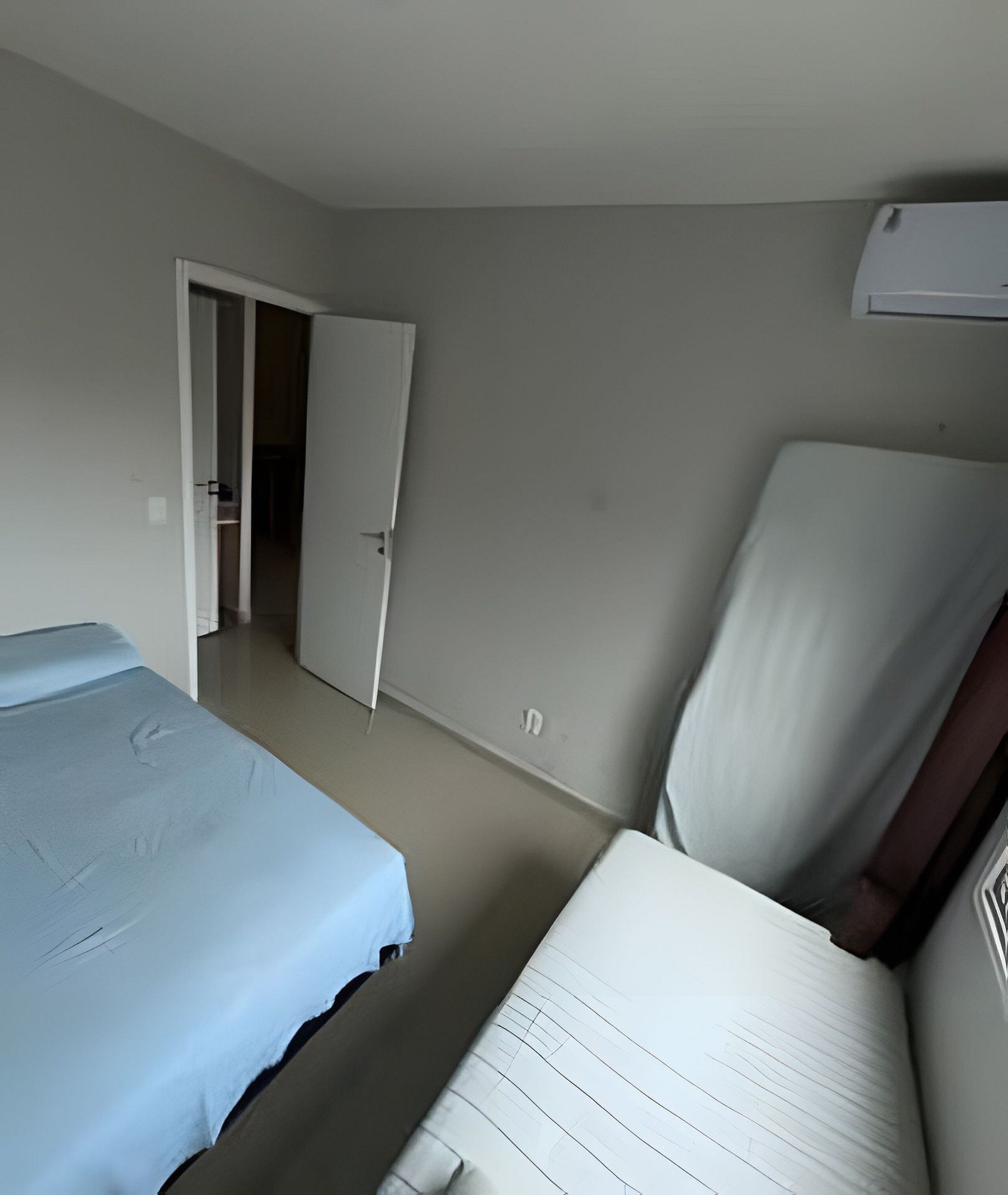 Une pièce comprenant un lit, une chaise, une porte donnant sur une autre pièce et un climatiseur fixé au mur.