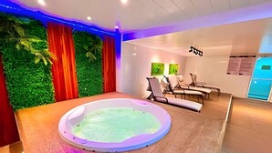 Una stanza spa con una vasca idromassaggio circolare, pavimento in legno e una parete verde con tende.